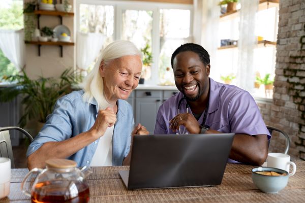 Une personne âgée consulte un ordinateur accompagnée d'un professionnel de l'aide à la personne