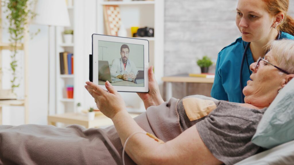 Résidente d'un EHPAD en téléconsultation sur une tablette avec un médecin accompagnée par une aide-soignante à son chevet