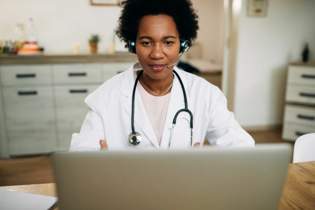 Femme médecin portant une blouse blanche, un stéthoscope et un casque avec micro en consultation de télémédecine sur son ordinateur portable