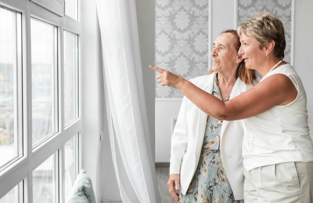 Une femme montre à une personne âgée la vue depuis la fenêtre de son futur EHPAD